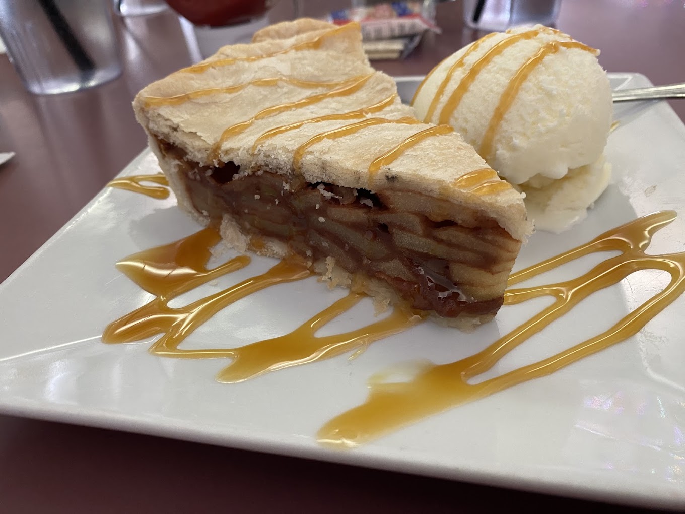 Slice of apple pie with vanilla ice cream and caramel drizzle