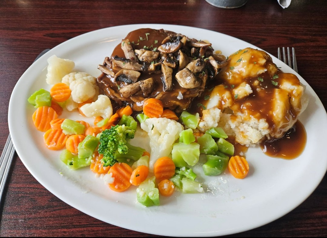 Salisbury steak smothered in mushroom gravy with mashed potatoes and steamed vegetables